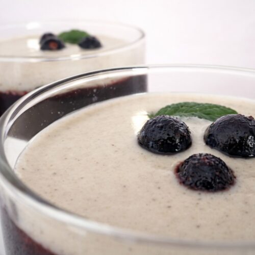 Nahaufnahme: Vegan-glutenfreies Beeren-Gelee im Glas, dunkle Beerenschicht und helle Creme, dekoriert mit Heidelbeeren und Minze