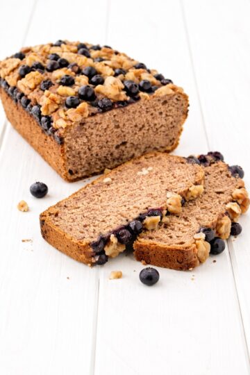 Angeschnittenes veganes Bananenbrot ohne Gluten mit Blaubeeren und Walnüssen auf weißem Untergrund