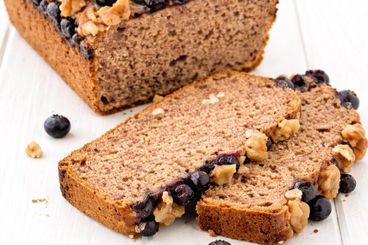 Angeschnittenes veganes Bananenbrot ohne Gluten mit Blaubeeren und Walnüssen auf weißem Untergrund