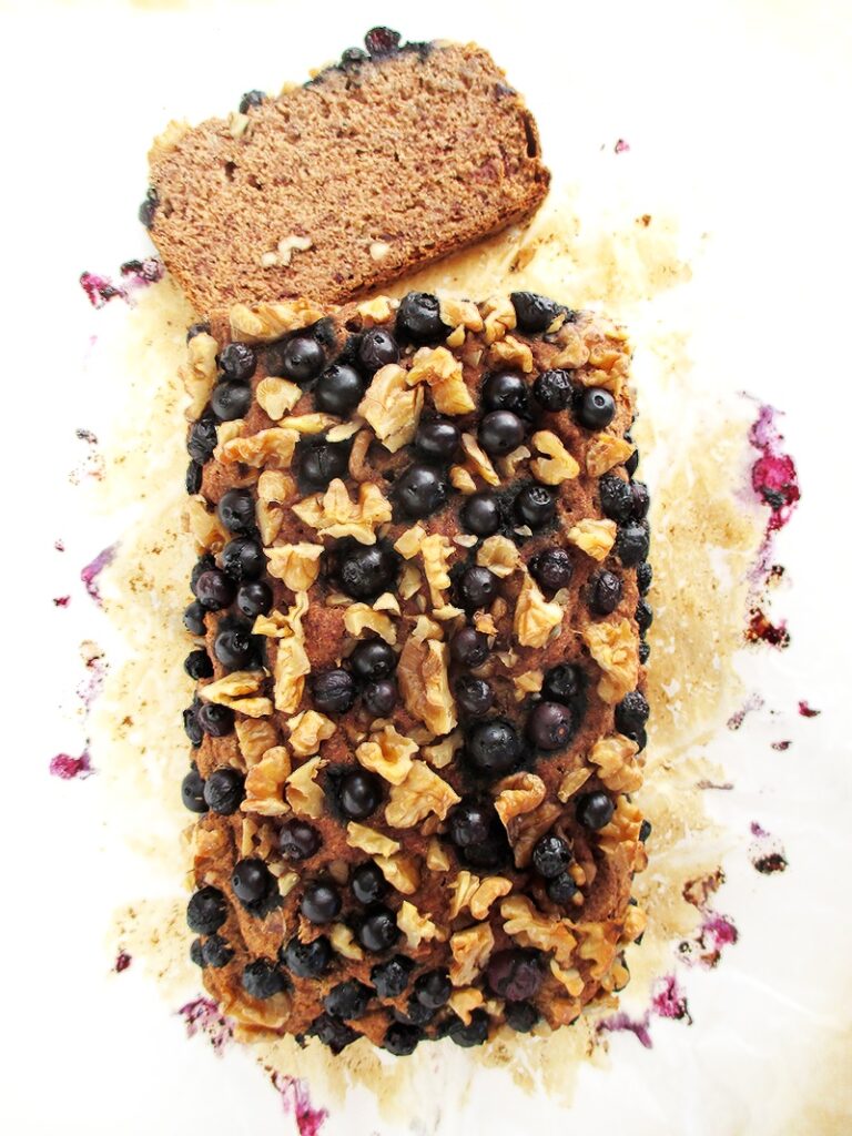 Vegan gluten-free banana loaf with blueberries and walnuts, sliced on a white surface