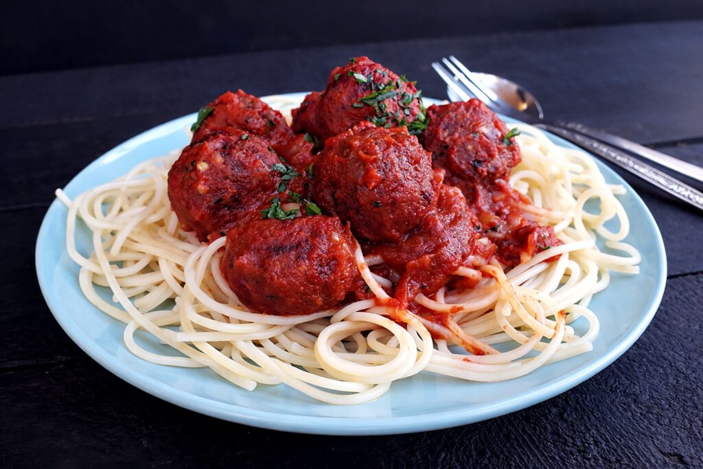 Veganes glutenfreies Fleischbällchen aus Buchweizen und Roter Bete auf einer Gabel mit Tomatensauce