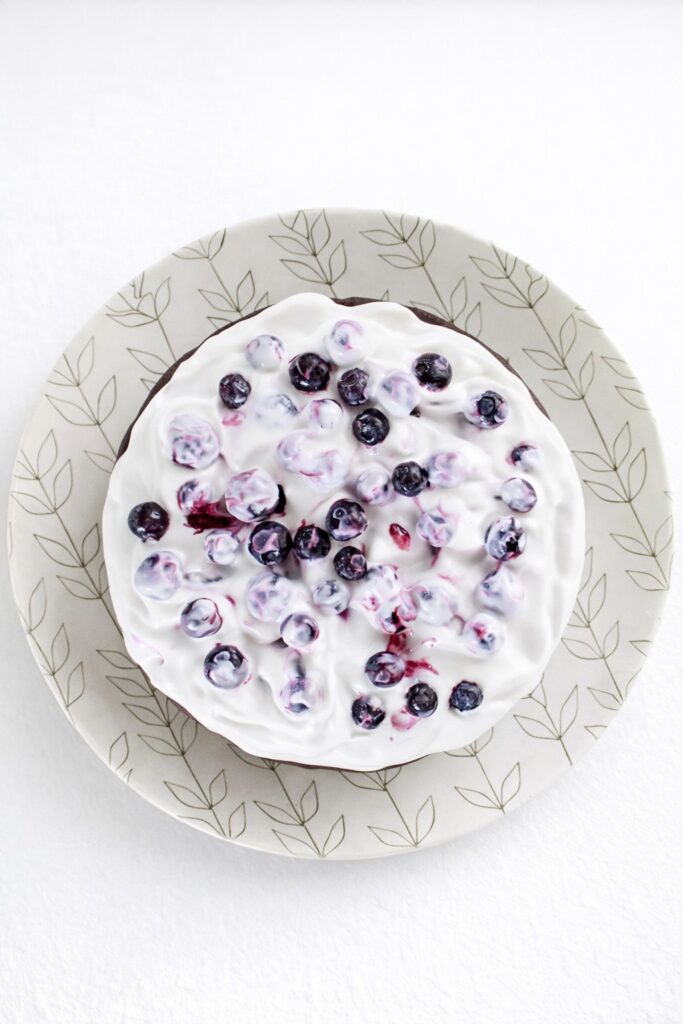 Overhead view of a whole vegan gluten-free chocolate cake with white topping and blueberries.