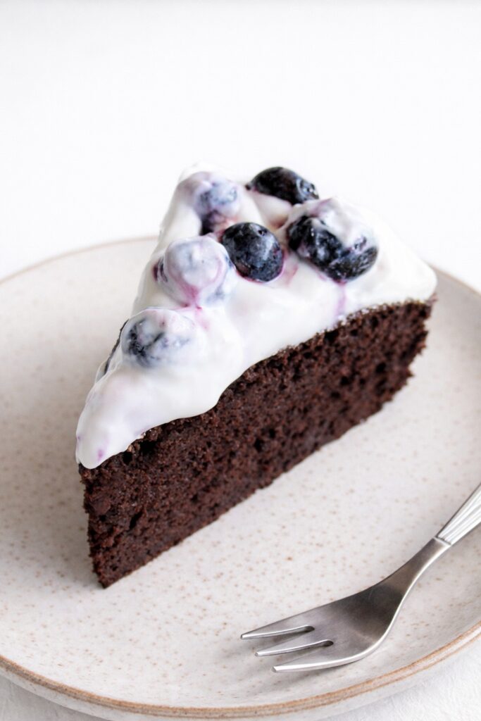 Vegan gluten-free chocolate cake slice topped with creamy yogurt and blueberries on a plate.