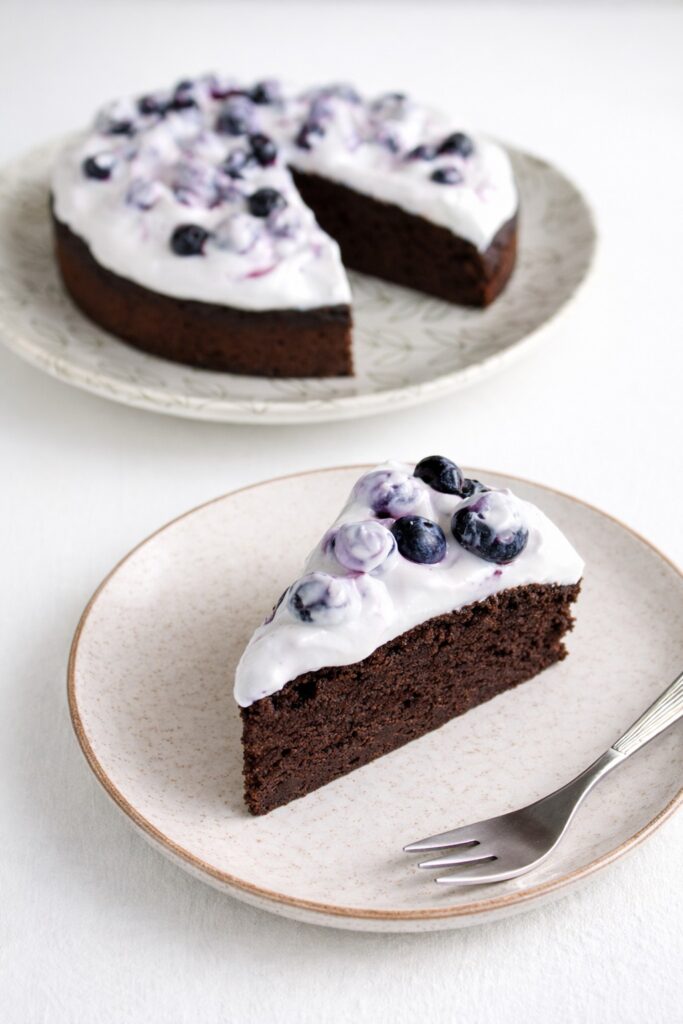 Vegan gluten-free chocolate cake with one slice removed on white table.