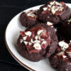 Vegan, gluten-free glazed hazelnut chocolate cookies garnished with hazelnut pieces, arranged on a plate.