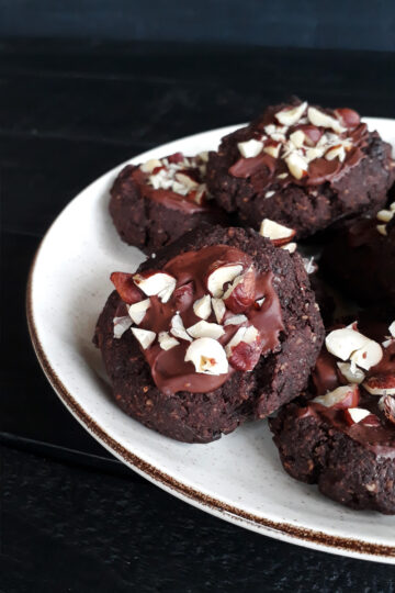 Vegane glutenfreie glasierte Haselnuss-Schoko-Cookies, garniert mit Haselnussstückchen, auf einem Teller angerichtet.