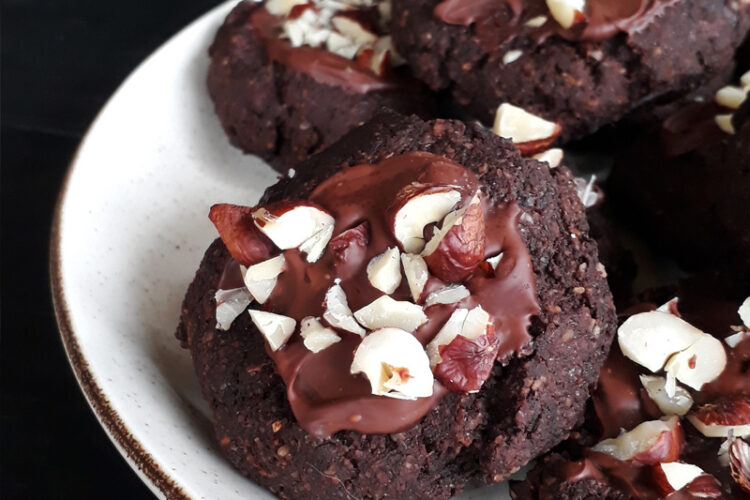Vegane glutenfreie glasierte Haselnuss-Schoko-Cookies, garniert mit Haselnussstückchen, auf einem Teller angerichtet.